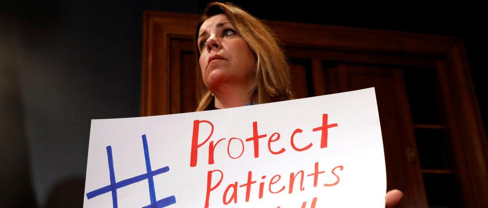 Eine Frau demonstriert mit einem Schild für den Erhalt der Krankenversicherung am Rande der Kongress-Beratungen.