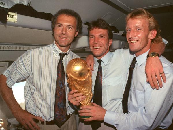 DFB-Teamchef Franz Beckenbauer, Kapitän Lothar Matthäus und Andreas Brehme präsentieren den Pokal auf dem Rückflug aus Rom. 