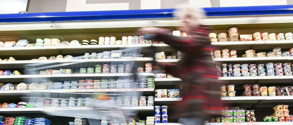 Eine Kundin geht in einem Supermarkt mit ihrem Einkaufswagen an einem Kühlregal vorbei. 