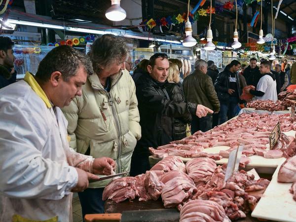 Käufer und Verkäufer stehen in Athen auf dem Fleischmarkt Varvakeios Agora an einer Fleischtheke. Zahlreiche Einwohner Athens versorgten sich vergangene Woche vor dem in Griechenland "Tsiknopempti" genannten Feiertag mit Fleisch Im Alltag können sich viele Kunden nur noch selten Fleisch leisten.