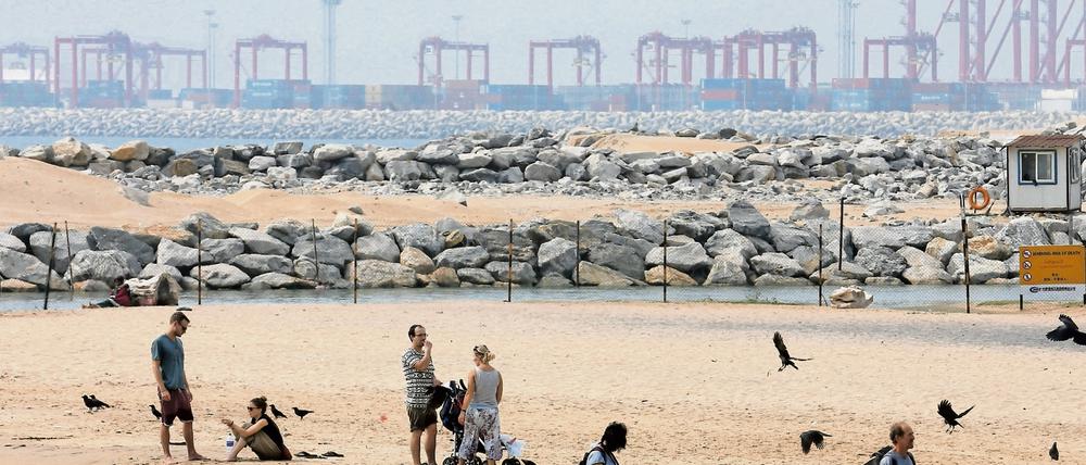 Zwischen Tourismus und Handel. Urlauber spazieren am Strand von Colombo in Sri Lanka, während im Hintergrund an der großen Hafen-City gebaut wird.