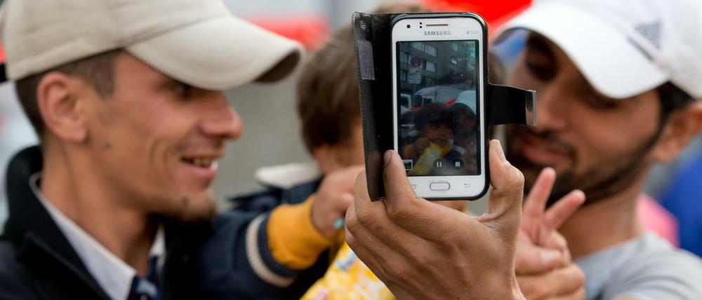 Zwei junge Männer mit einem kleinen Jungen auf dem Arm halten ein Smartphone in die Kamera.