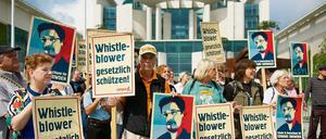 Menschen stehen vor dem Bundeskanzleramt und halten Schilder hoch, auf denen politisches Asyl für Edward Snowden gefordert wird.