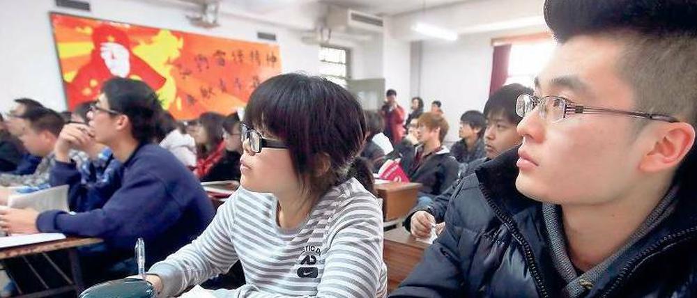 In einer Universität in Peking sitzen Studierende im Seminarraum, im Hintergrund ein Wandbild von Lei Feng, Soldat der chinesischen Volksbefreiungsarmee.