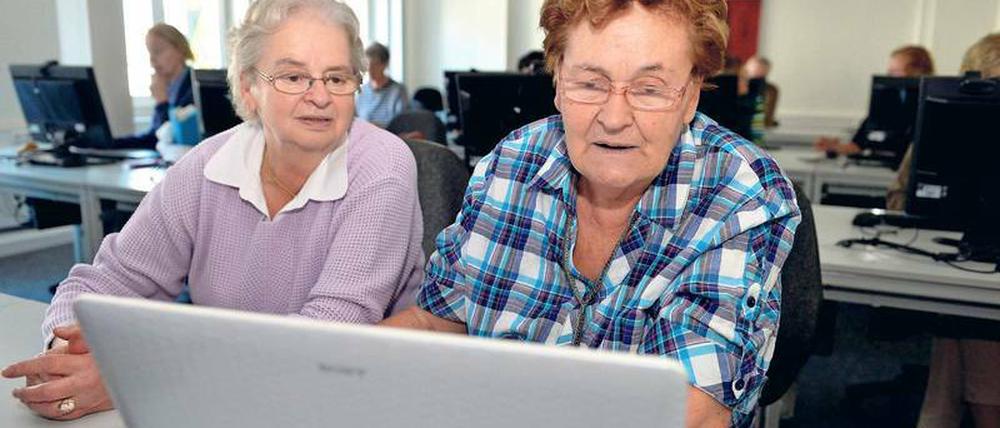 Zwei ältere Frauen sitzen in einem Klassenraum vor einem Laptop.