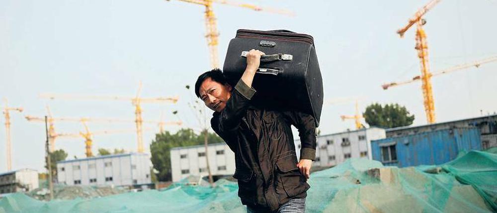 Ein Mann, der einen Koffer auf dem Rücken trägt, geht über eine Baustelle.