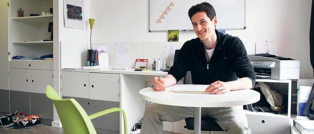 Ein junger Mann sitzt in einem modern eingerichteten Appartement an einem Tisch.