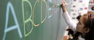 Ein Mädchen schreibt das ABC mit farbiger Kreide in Großbuchstaben auf eine Tafel.