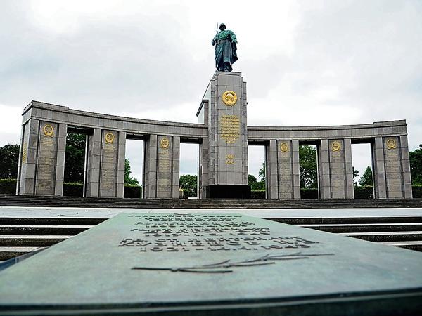 Das Sowjetische Ehrenmal in Berlin: Die Skulptur eines Soldaten steht auf einem hohen Sockel, der Teil einer Arkade mit den Namen getöteter Soldaten ist. Im Vordergrund eine Gedenktafel.