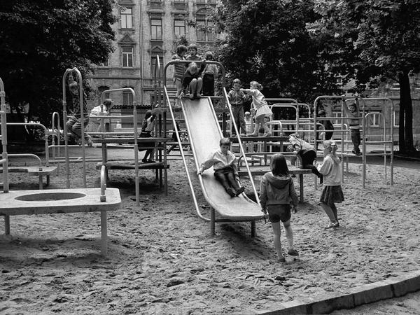 Kinder spielen auf einem Spielplatz mit Klettergerüsten und einer Rutsche aus Metall.