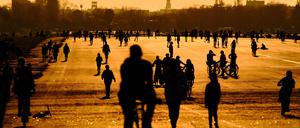 Menschen gehen im Licht der untergehenden Sonne über das Tempelhofer Feld.