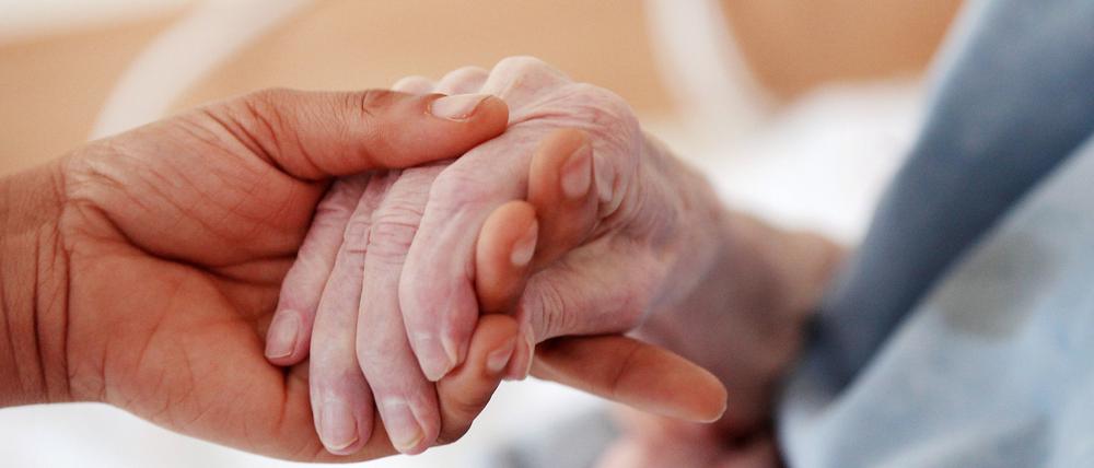 Eine Betreuerin hält die Hand einer älteren Frau.