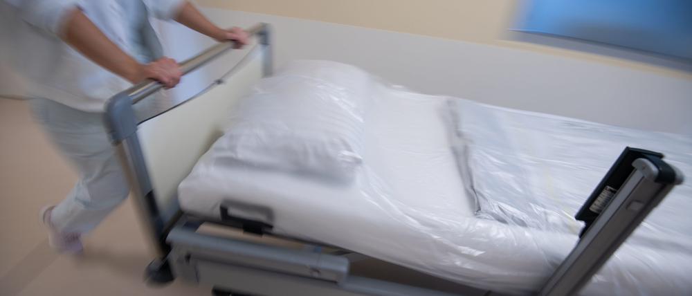 Eine Krankenpflegerin schiebt ein Bett durch einen Gang einer Station.