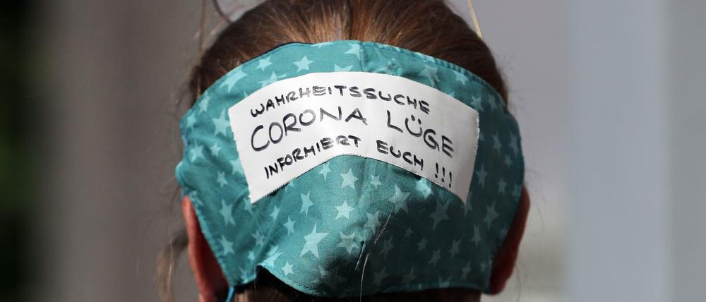 Eine Demonstrantin trägt eine Maske auf dem Hinterkopf am Rande der Demo auf dem Rosa-Luxemburg-Platz.