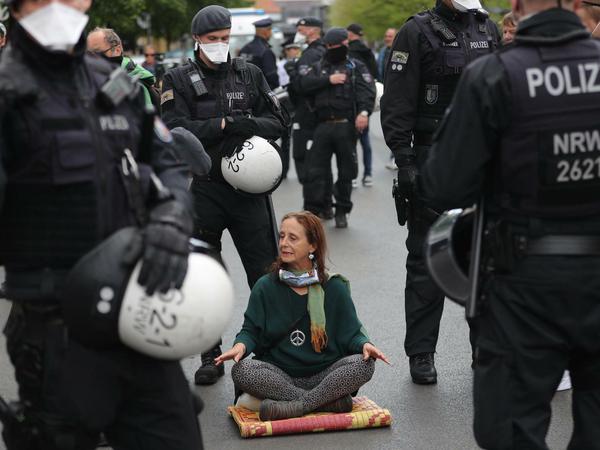 Eine Frau sitzt am Rande einer Demonstration umringt von Polizisten auf der Straße. Die Gruppe "Demokratischer Widerstand" wollte auf dem Rosa-Luxemburg-Platz gegen die strikten Kontaktbeschränkungen in der Coronakrise demonstrieren.