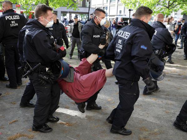 Ein Demonstrant wird von Polizisten mit Mundschutz am Rande der Demonstration am Rosa-Luxemburg-Platz abgeführt.
