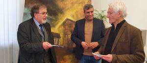 Mario Marcus (links), Schatzmeister der Gemeinde, übergibt ein Buch über die alte Synagoge an den Schenker des Gemäldes, Werner Brunner. Im Hintergrund: SPD-Chef Raed Saleh.
