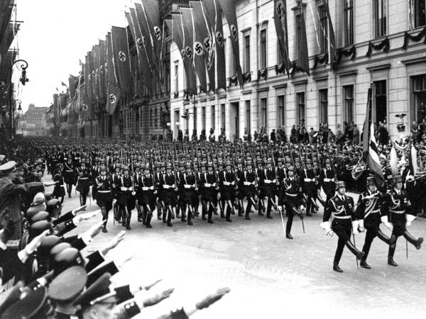 SS-Mitglieder marschieren am 20. April 1939 an Adolf Hitler, der seinen rechten Arm zum Gruß erhoben hat (Bildrand links), vorbei. 