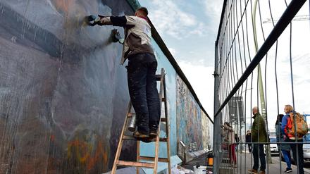 Ein Arbeiter entfernt hinter einem Bauzaun Graffitis von einem Bild auf der ehemaligen Berliner Mauer.