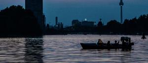 Ein Motorboot fährt abends auf der Spree. Im Hintergrund sind Allianz-Tower und der Fernsehturm zu sehen.
