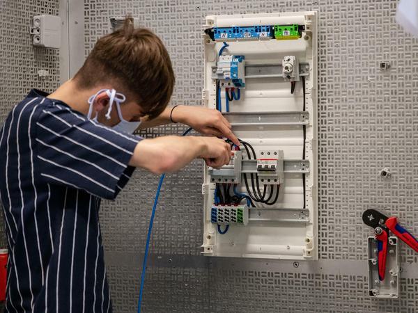 Ein Auszubildender der Elektrotechnik montiert in einer Werkstatt einen Sicherungskasten. 