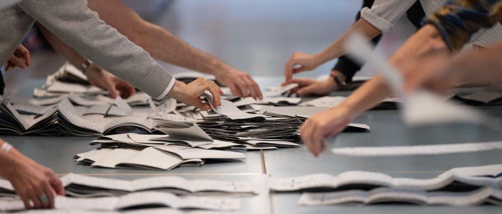 Hände von Wahlhelfern und Wahlhelferinnen auf einem Tisch beim Zählen von Stimmzetteln in einem Wahllokal.