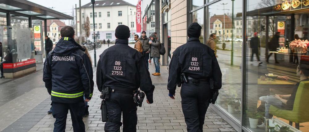 Ein Mitarbeiter des Ordnungsamtes und zwei Beamte der Bereitschaftspolizei gehen auf Streife vor dem Einkaufszentrum in Cottbus (Brandenburg).