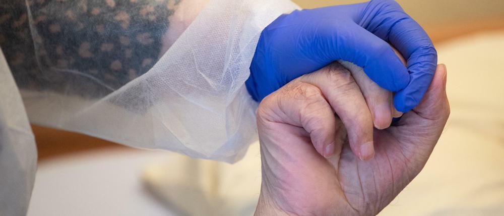 Eine Altenpflegerin in Schutzausrüstung hält die Hand eines Bewohners. (Symbolbild)