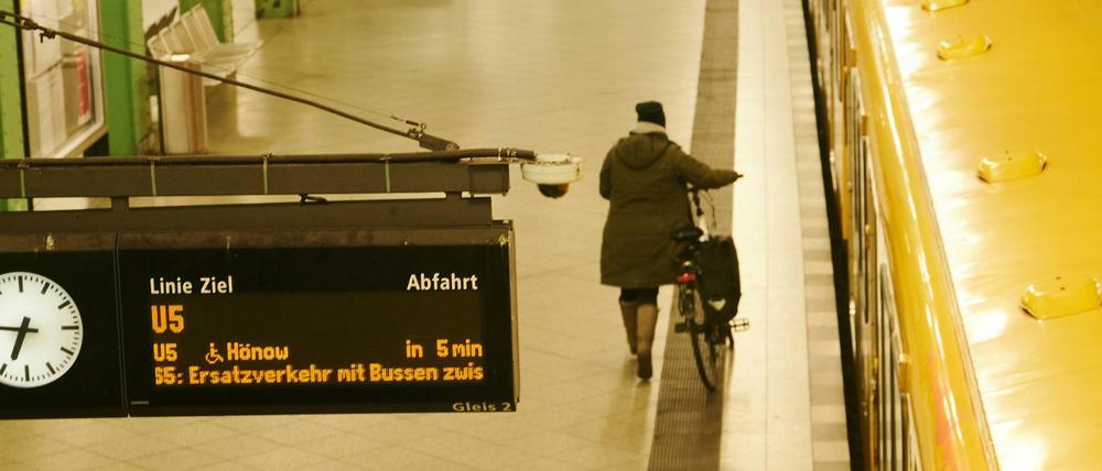 Eine Frau läuft am Alexanderplatz mit dem Fahrrad an einer U-Bahn entlang.