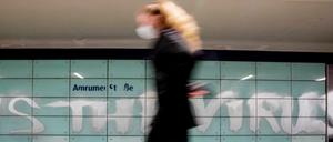 Eine Frau mit Mund-Nasen-Schutz geht am U-Bahnhof Amrumer Straße in Berlin an einem Graffiti vorbei.