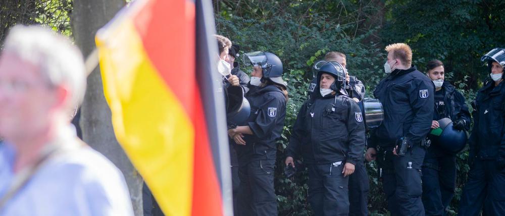 Polizisten stehen bei einer Kundgebung gegen die Corona-Beschränkungen auf der Straße des 17. Juni hinter einem Teilnehmer mit Deutschland-Flagge. Die Polizei hat die Veranstaltung kurz vor Ende doch noch aufgelöst.