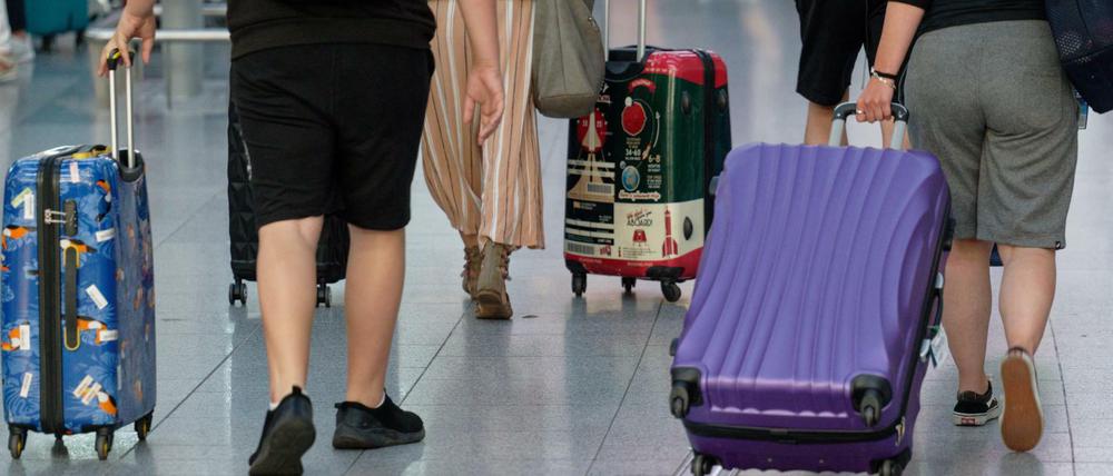 Reisende gehen ein einem Flughafen mit Koffern durch die Abflughalle.