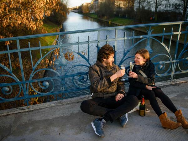 Ein Paar sitzt auf einer Brücke über dem Landwehrkanal und trinkt Sekt. 