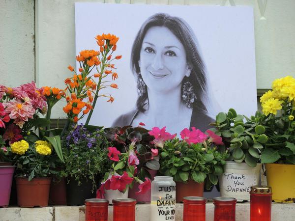 Kerzen und Blumen stehen vor einem Foto der ermordeten Journalistin Caruana Galizia.