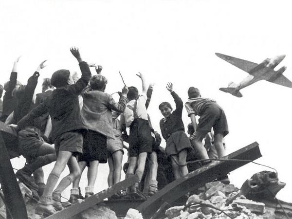 Westberliner Jungs stehen 1948 auf einem Trümmerberg und begrüßen ein US-amerikanisches Transportflugzeug. 