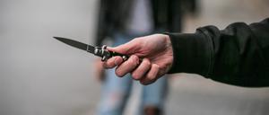 Männerhand mit einem verbotenen Springmesser auf der Straße.