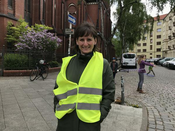 Katrin Andrzejewski steht in gelber Weste neben der Samariterkirche, sie ist eine der Kiezlotsinnen in Friedrichshain.