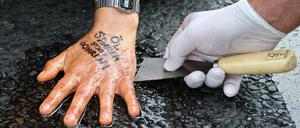 Ein Polizist löst die festgeklebte Hand eines Aktivisten der "Letzten Generation" in Berlin. Auf der Hand steht der Slogan "Öl sparen statt bohren".