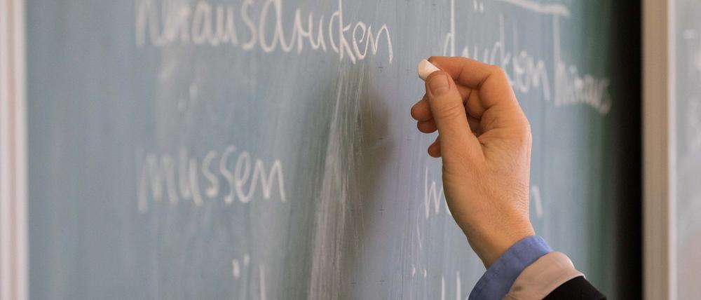 Eine Lehrerin steht in einem Klassenraum an einer Tafel und schreibt.