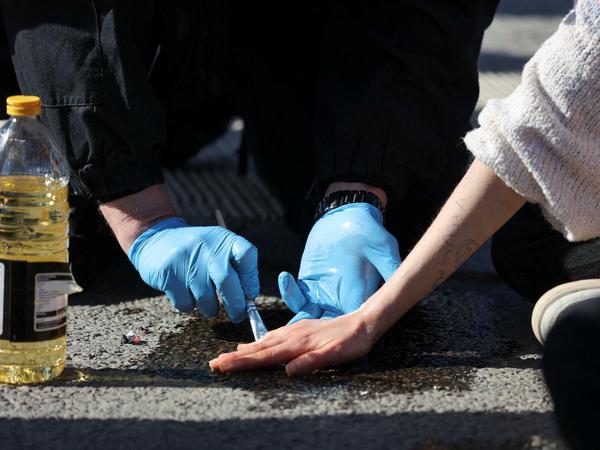 Ein Polizist versucht, die festgeklebte Hand einer Aktivistin der "Letzen Generation" mit Sonnenblumenöl vom Asphalt zu lösen. 