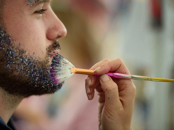 Ein Besucher lässt sich während des Lollapalooza Festivals im Olympiapark von einer Schaustellerin den Bart mit Glitzer verzieren.