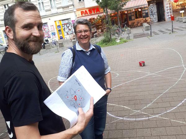 Luke, ein ehrenamtlicher Helfer aus der Nachbarschaft, zeigt Bezirksbügermeisterin Monika Hermann die Pläne für eine permanente Bemalung auf dem Asphaltboden des "Platz ohne Namen" in Friedrichshain-Kreuzberg.