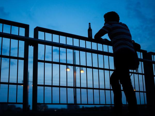 Die Silhouetten eines Mannes und einer Bierflasche zeichnen sich am 29.06.2015 auf der Warschauer Brücke in Berlin vor dem Abendhimmel ab.