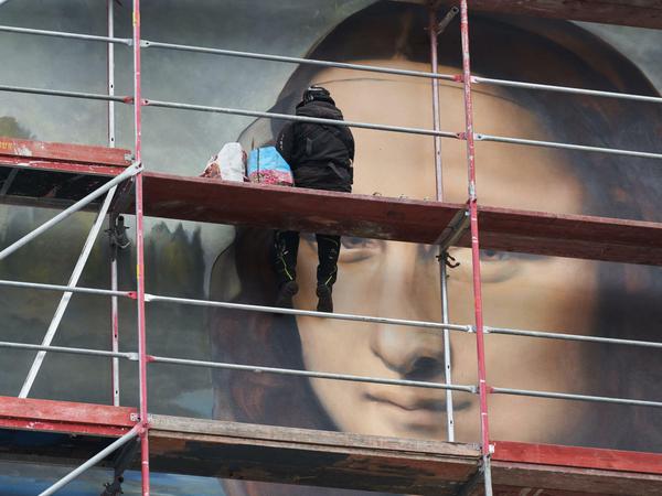 21.02.2019, Berlin: Ein Sprayer vollendet, auf dem Gerüst sitzend, das riesige Wandbild von Da Vincis Mona Lisa.