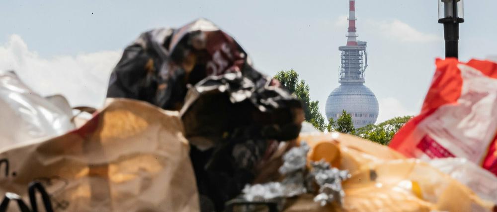 Der Berliner Fernsehturm ragt hinter einem vollen Mülleimer im Volkspark Friedrichshain hervor. 