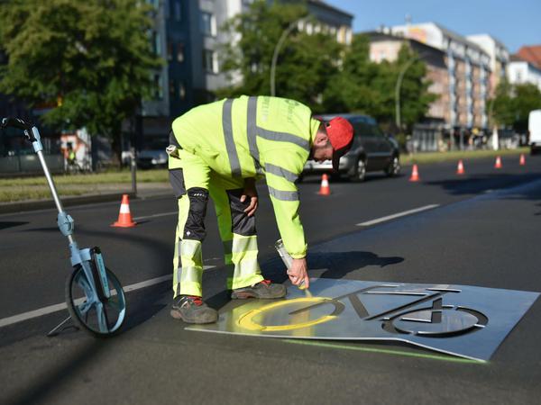 Verkehrswende durch Coronakrise: Ein Bauarbeiter sprüht ein Fahrradsymbol auf die Frankfurter Allee.