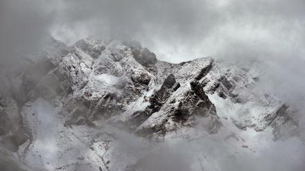 Die verschneiten Alpen sind durch eine Wolkenlücke zu sehen.