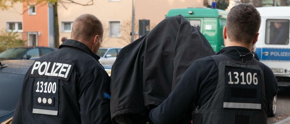 Polizeibeamte führen mit Handschellen einen festgenommenen Mann nach einer Razzia in einem Wohnhaus in Tempelhof ab.