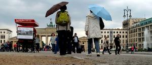 Passanten schützen sich am Brandenburger Tor mit Schirmen vor dem Regenwetter.