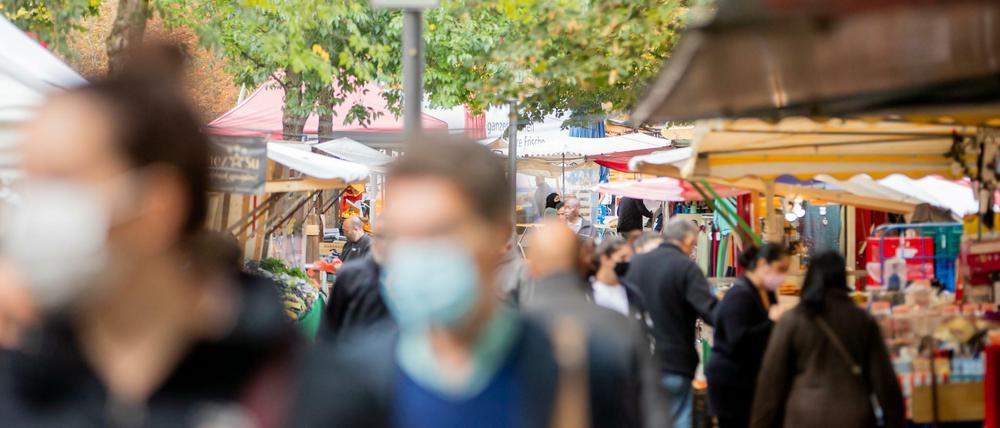 Menschen mit Mundschutz gehen in Berlin-Kreuzberg über den Markt am Maybachufer.